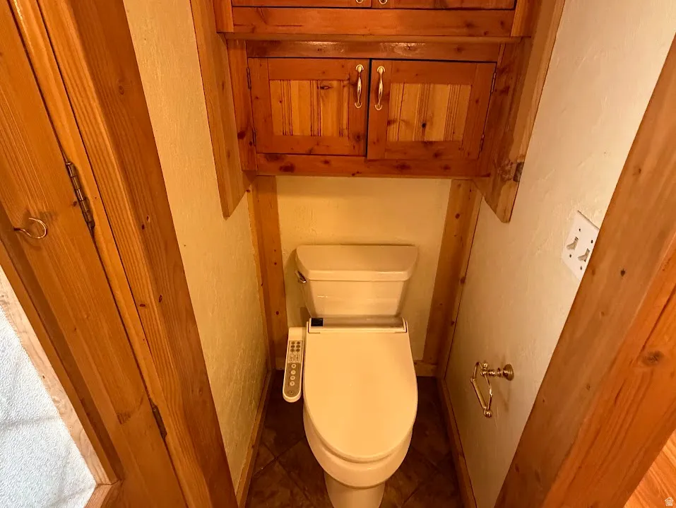 Powder room featuring a bidet toilet, wood-finish wall paneling, tile flooring, and integrated wood cabinetry with metal hardware