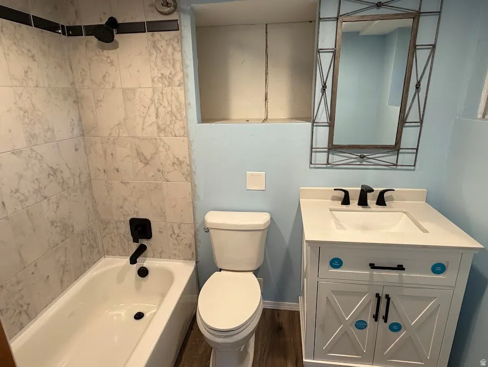 Bathroom featuring a white vanity with a rectangular sink and matte black faucet, a white toilet, and a white bathtub with marble-look wall tiling