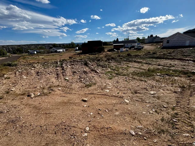 Expansive land parcel featuring existing ground cover, a partial dirt road, and visible distant structures