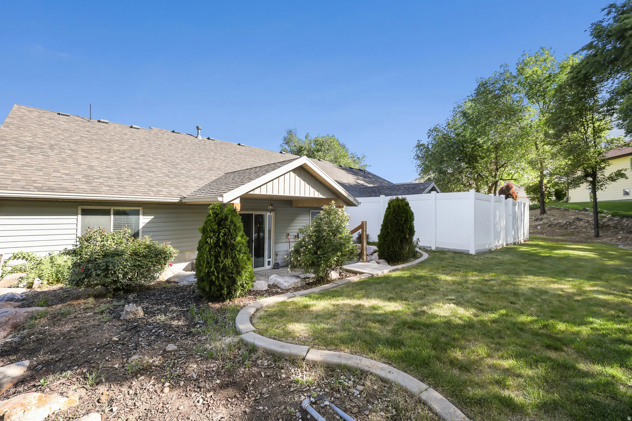 Expansive backyard featuring a green lawn, white privacy fencing, and mature trees