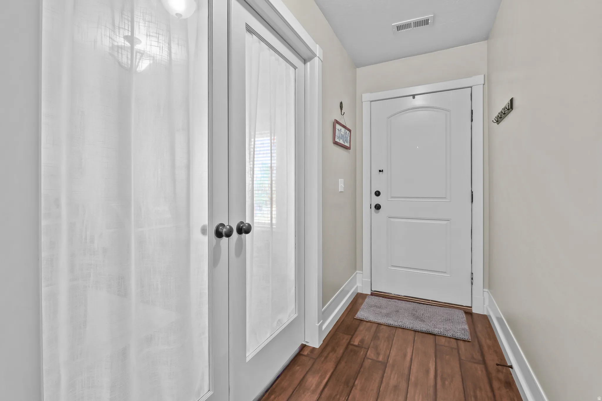 Foyer featuring a white paneled entry door, wood-finish flooring, white baseboards, and light-toned walls
