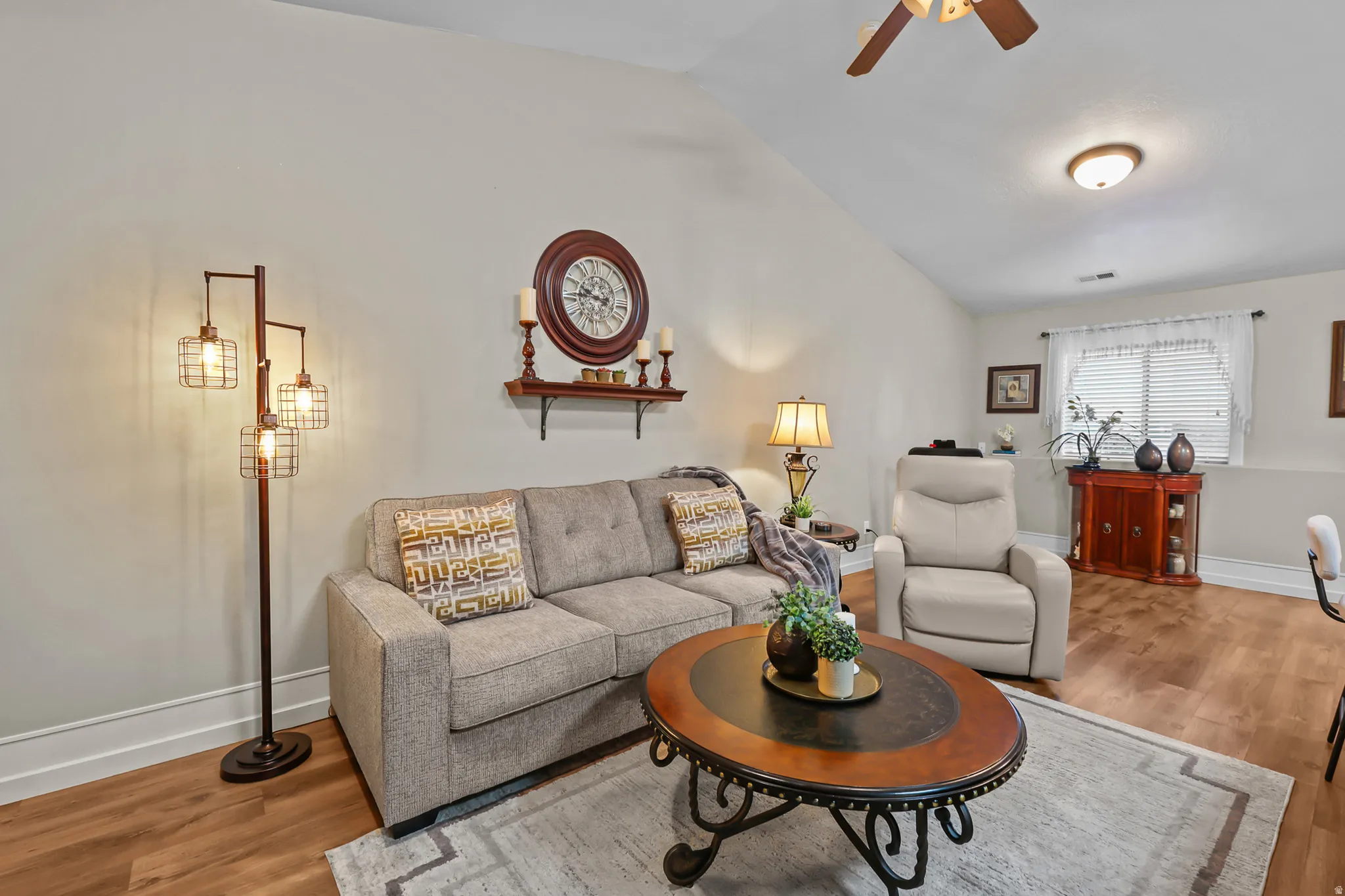 Living area featuring vaulted ceilings, wood-finish flooring, a window with blinds and curtains, and a built-in ceiling fan