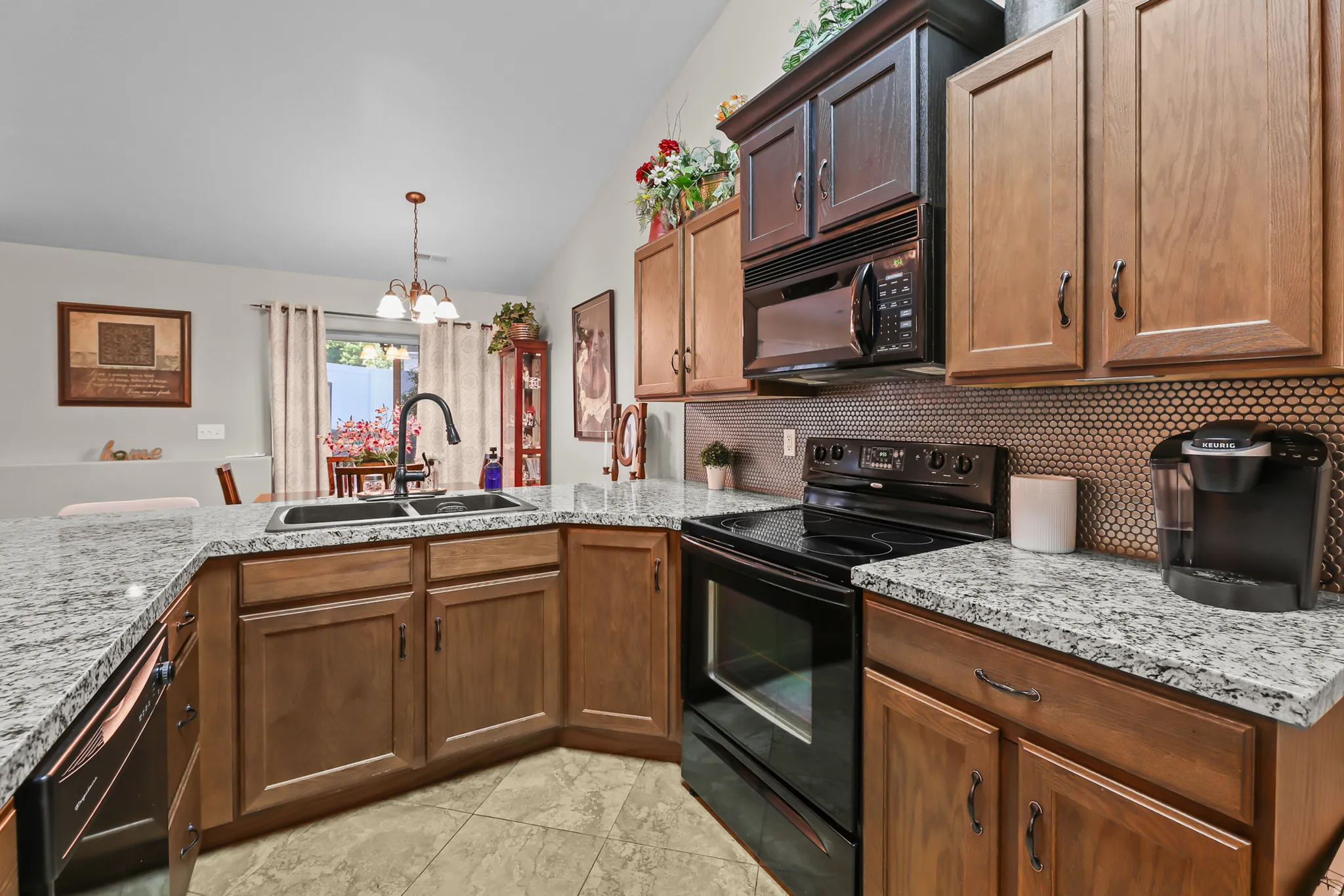 Kitchen featuring granite-style countertops, wood cabinetry, a dual basin sink with a gooseneck faucet, black appliances, and a geometric pattern backsplash
