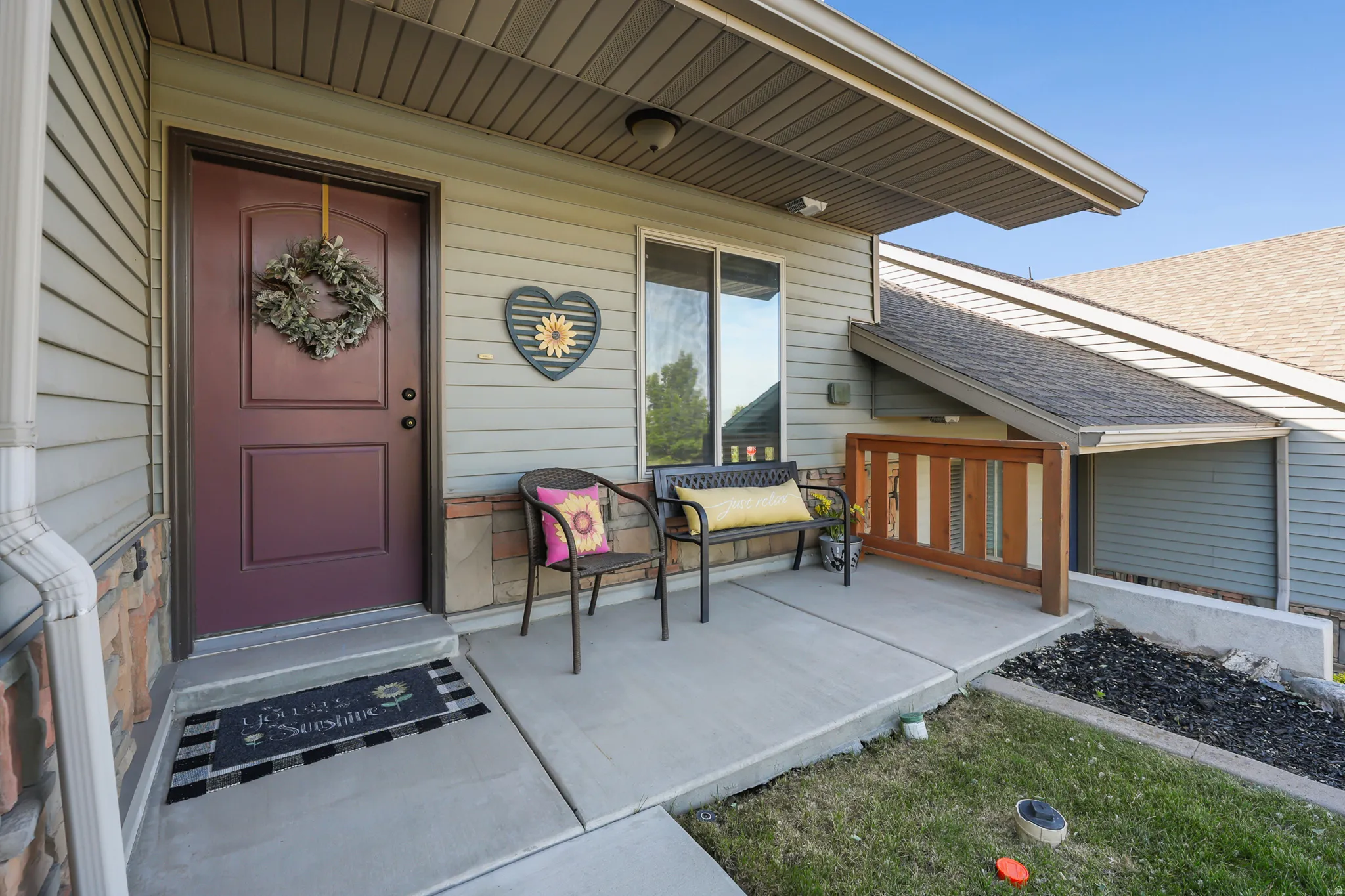 Entryway featuring a rich maroon door, light gray siding, stone veneer accents, a concrete porch, and a wood-panelled railing