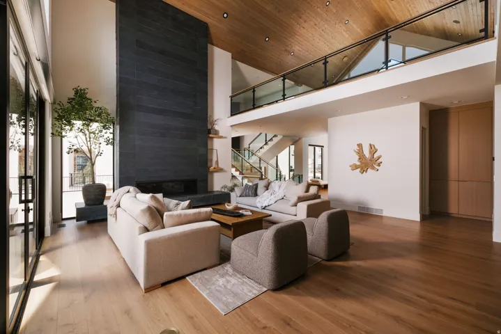Open-concept living space featuring a floor-to-ceiling dark stone fireplace, high vaulted wood-paneled ceilings, and light wood-finish flooring