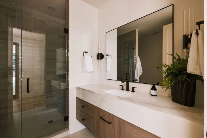 Contemporary bathroom featuring a glass-enclosed shower with horizontal tile, a floating wood-finish vanity with a single basin, a white countertop, and matte black fixtures