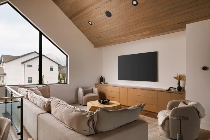 Vaulted wood-paneled ceiling, large angular window, built-in wood cabinetry, recessed lighting, and a glass-paneled railing