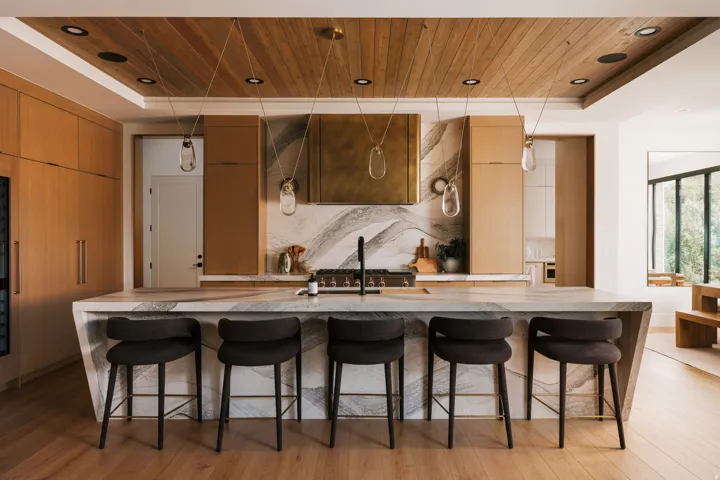 Open-concept kitchen featuring a waterfall island with integrated seating, a wood-paneled ceiling with recessed lighting, a stone slab backsplash, and light wood-finish cabinetry