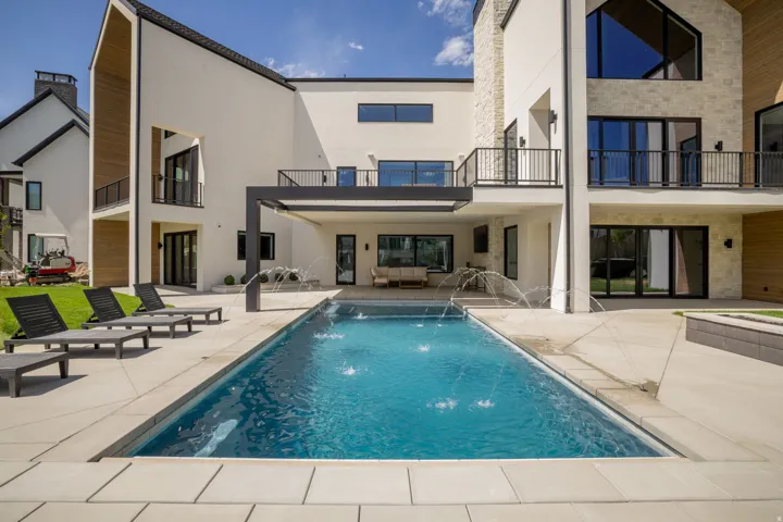 Contemporary rear exterior featuring an in-ground swimming pool with water features, extensive patio space, and multiple balconies