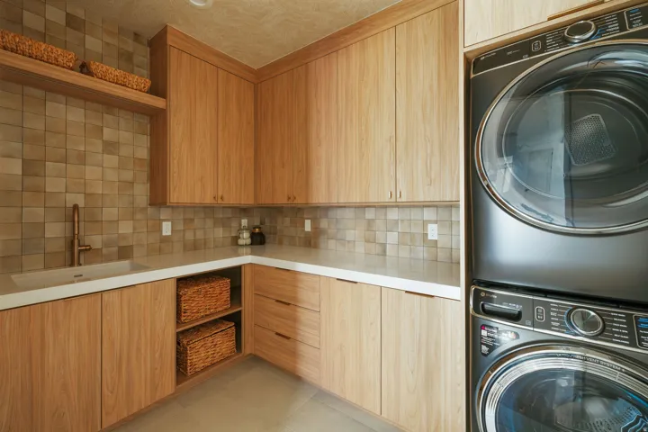 Laundry area featuring light wood-finish cabinetry, white countertops, and a tiled backsplash