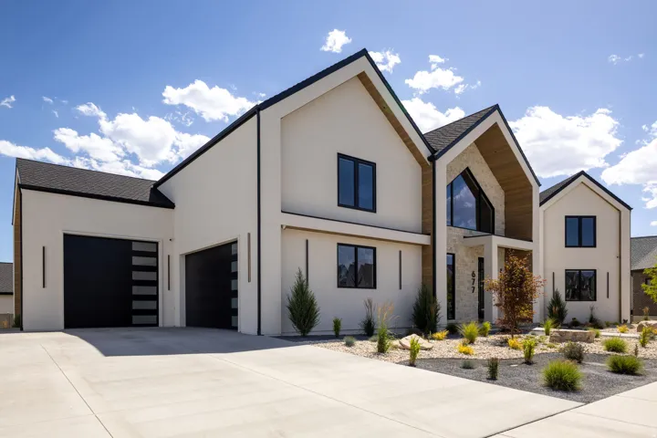 Modern architectural exterior featuring a light-colored stucco finish, contrasting black-framed windows, a prominent gable roofline, and a stone facade accent at the entry