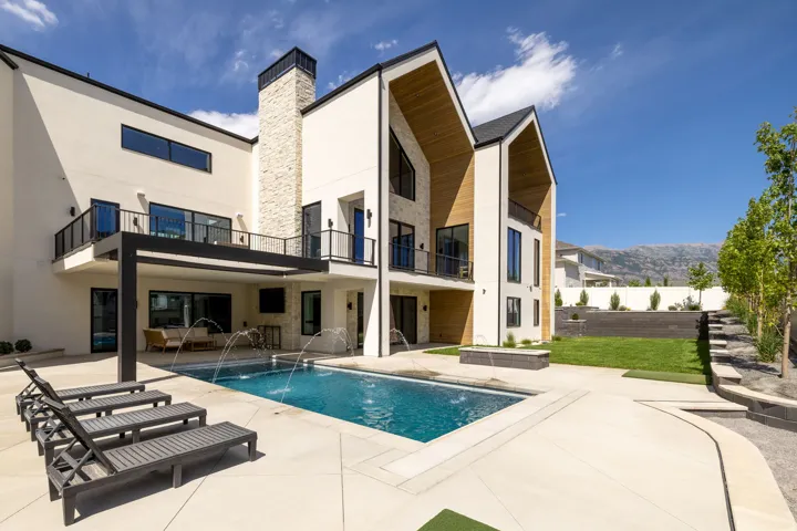 Contemporary exterior featuring a private swimming pool, concrete patio, a stone chimney, and multiple balconies with dark railings