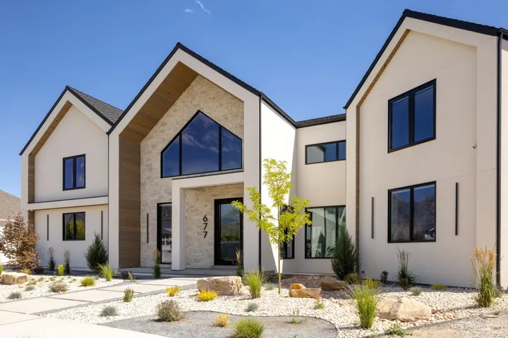 Modern facade featuring a prominent stone accent wall, expansive black-framed windows, and a clean stucco finish