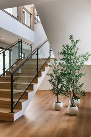 Multi-level interior featuring wood-finish flooring, a contemporary staircase with wood treads, glass balusters, and dark metal handrails