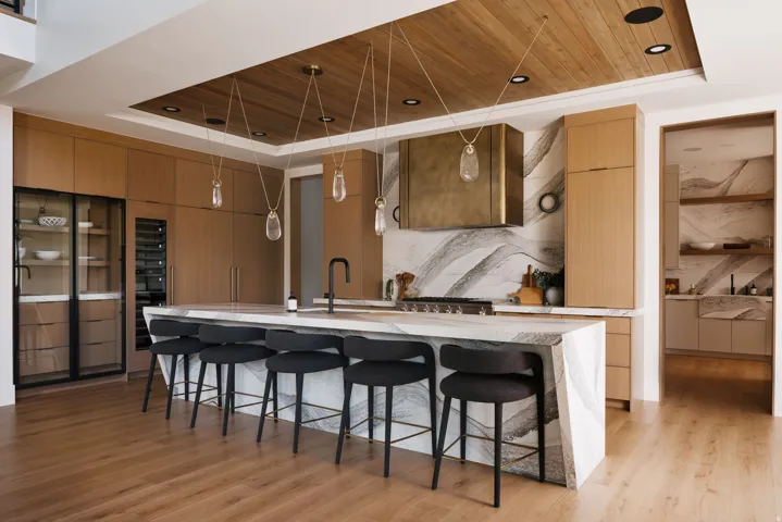 Gourmet kitchen featuring a waterfall island with integrated seating, custom wood cabinetry, a built-in wine cooler, a designer range hood, and wood-finish flooring