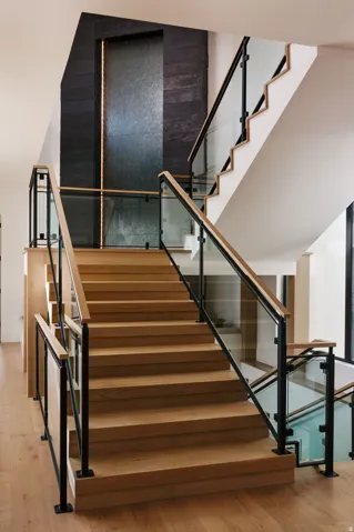 Hardwood staircase with glass and black metal railings, featuring a dark stone-clad accent wall with an integrated vertical light fixture