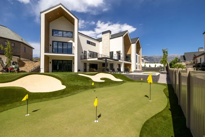 Expansive backyard featuring an artificial turf putting green with sand traps, a multi-level patio, and a privacy fence