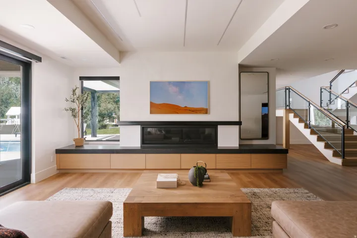 Living area featuring a sleek fireplace with a dark stone hearth and light wood cabinetry, wide plank wood-finish flooring, and a modern glass and wood staircase