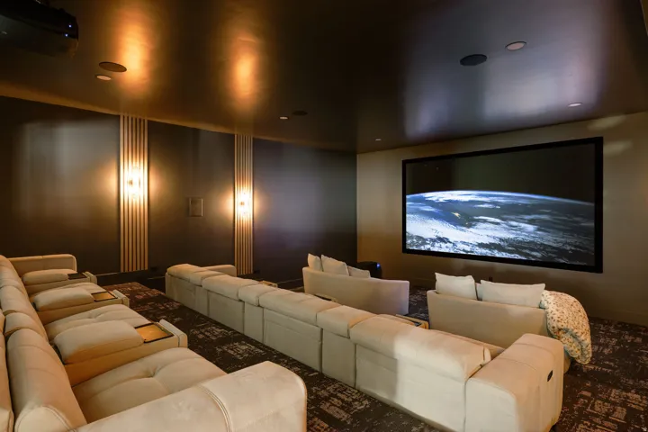 Dedicated media room featuring a large projection screen, recessed ceiling speakers, and wall-mounted sconces