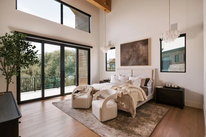 Spacious interior featuring a high vaulted ceiling with exposed wood beams, expansive floor-to-ceiling sliding glass doors, upper transom windows, recessed wall windows, and wood-finish flooring