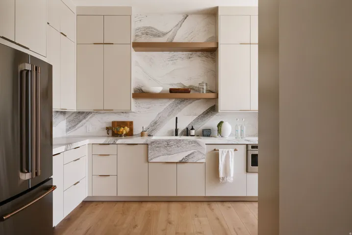 Modern kitchen featuring wood-finish flooring, light-toned flat-panel cabinetry, a stainless steel refrigerator, stone countertops, and a full-height stone slab backsplash