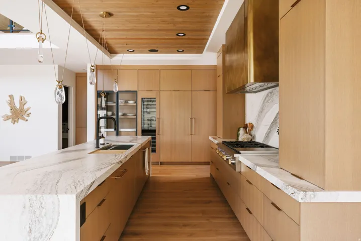 Gourmet kitchen featuring a substantial island with integrated sink, wood-finish flooring, custom wood cabinetry, stainless steel range with brass hood, and integrated refrigeration