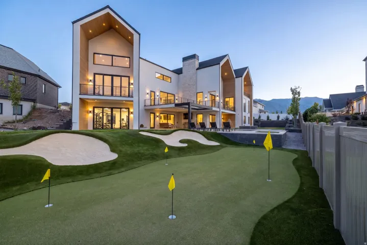 Rear exterior featuring multiple balconies, extensive dark-framed windows, and a golf putting green with sand traps