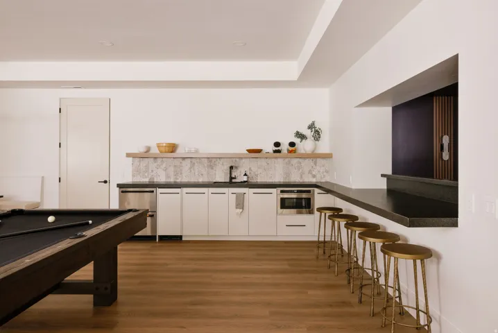Recreational space featuring wood-finish flooring, a built-in wet bar with white cabinetry, stainless steel microwave, and a black countertop with a pass-through opening