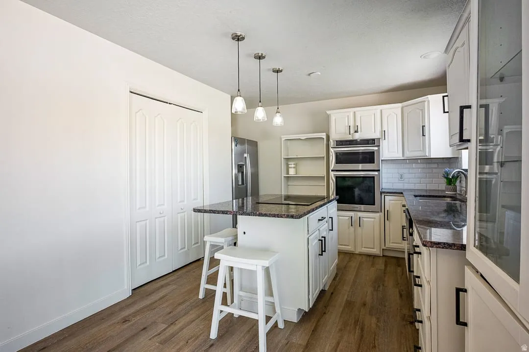 Kitchen featuring white cabinetry, dark granite countertops, stainless steel appliances, wood-finish flooring, and a subway tile backsplash
