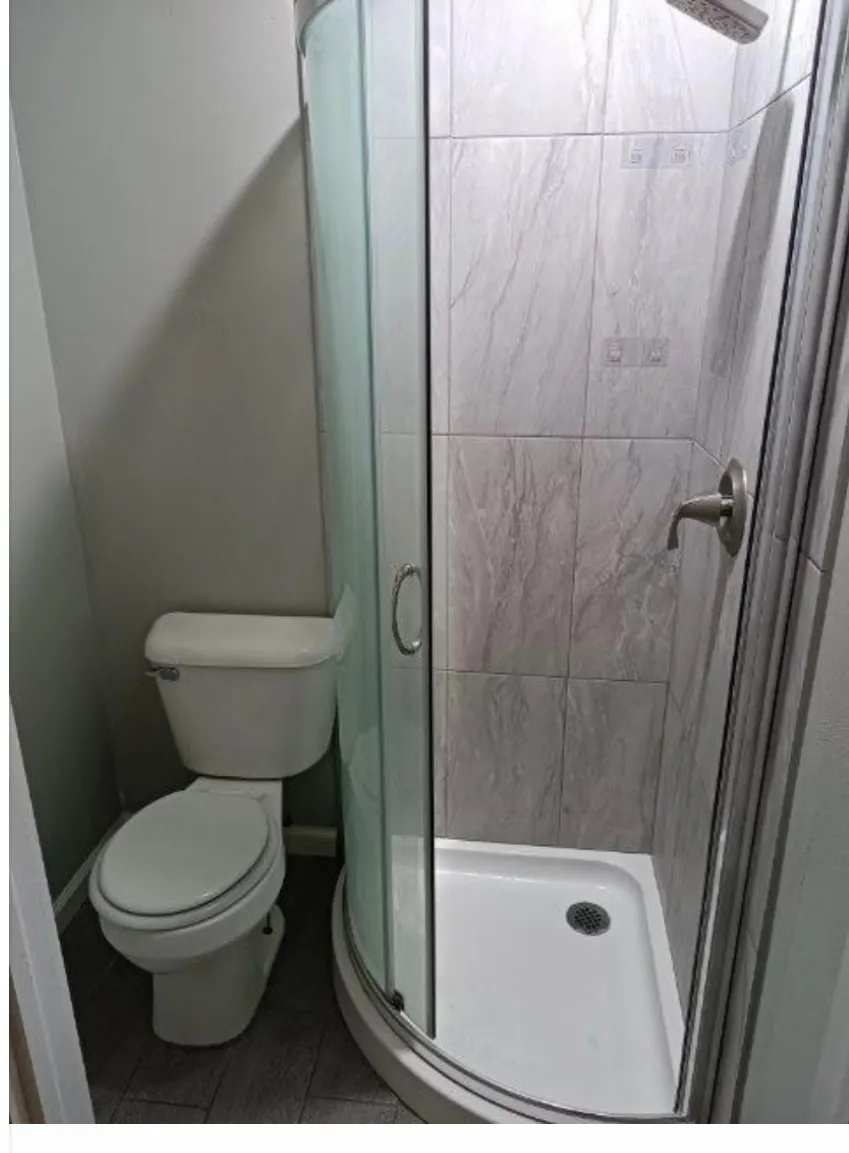 Compact bathroom featuring a curved glass shower enclosure with a white base and a brushed nickel showerhead