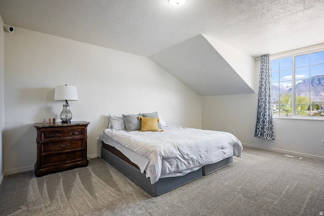 Spacious room featuring sloped ceilings, plush gray carpeting, and a large window offering mountain scenery