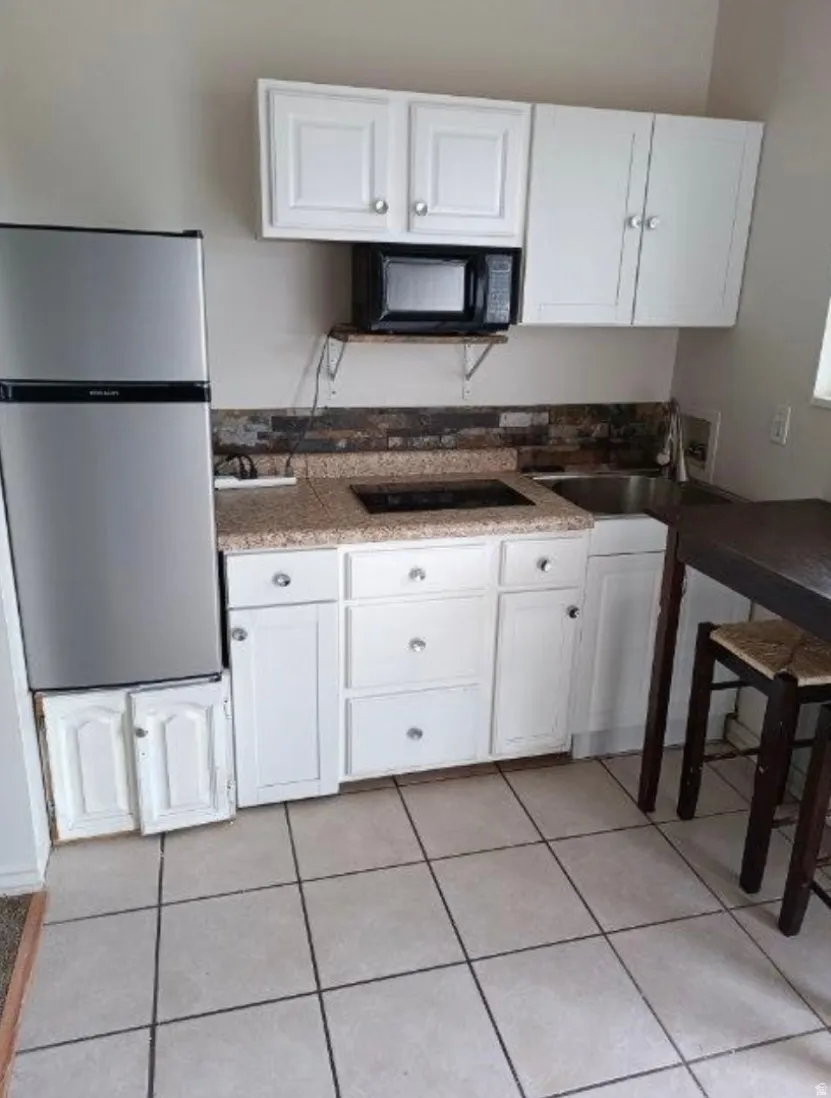 Compact kitchen featuring white cabinetry, a built-in microwave, integrated cooktop, a stainless steel refrigerator, and tiled flooring