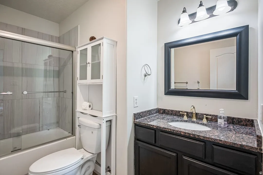 Bathroom featuring a built-in shower-over-tub with sliding glass doors, a vanity with a dark wood-finish cabinet, a speckled countertop, and a framed mirror
