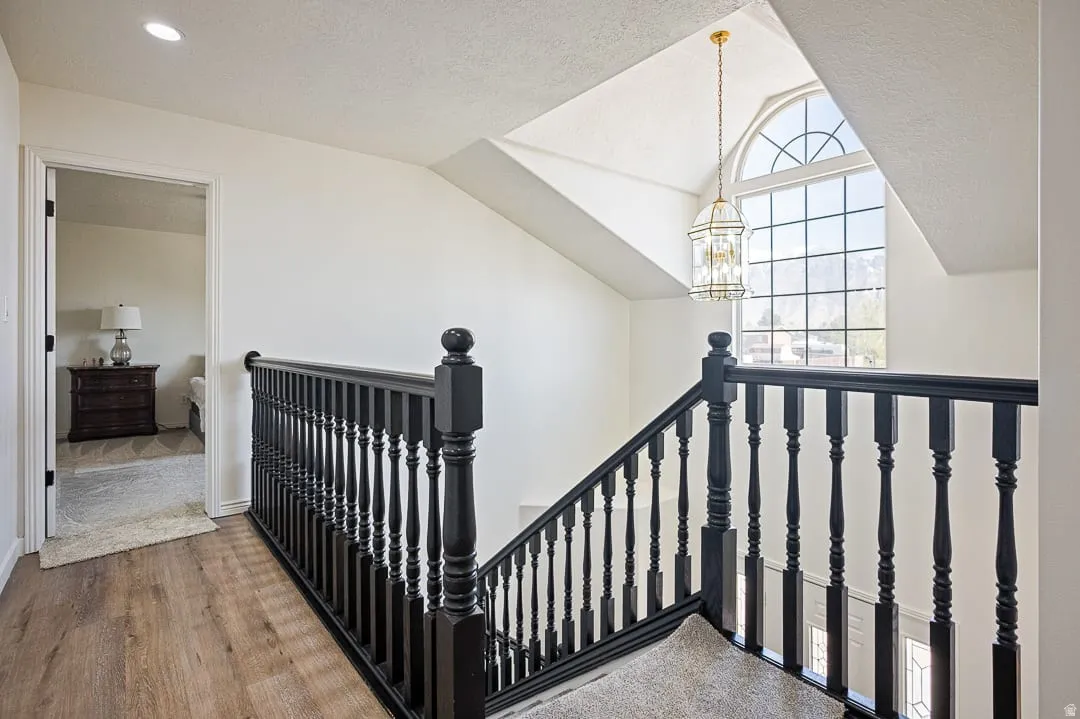 Upper landing featuring a striking arched window, a decorative pendant light fixture, wood-finish flooring, recessed lighting, and black balusters
