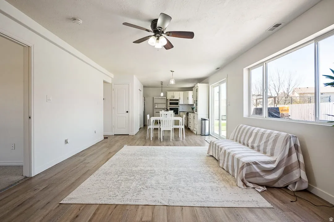Spacious open-concept living area featuring wood-finish flooring, ample natural light from large windows, and a modern ceiling fan