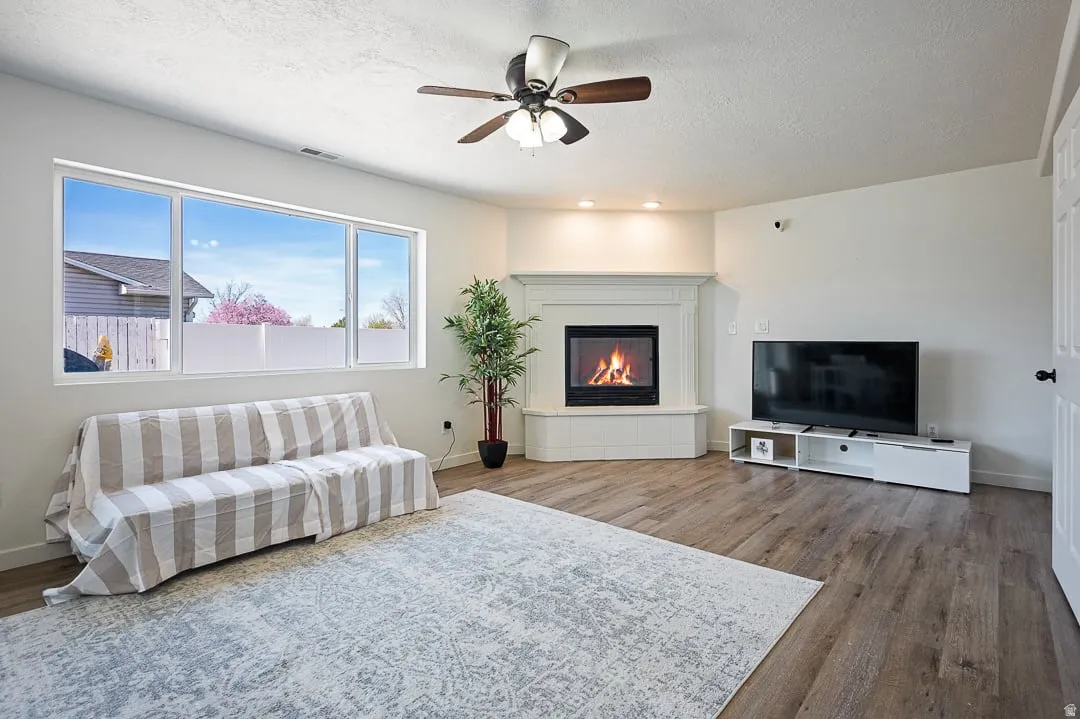 Living room featuring wood-finish flooring and a corner fireplace with a white mantel and hearth