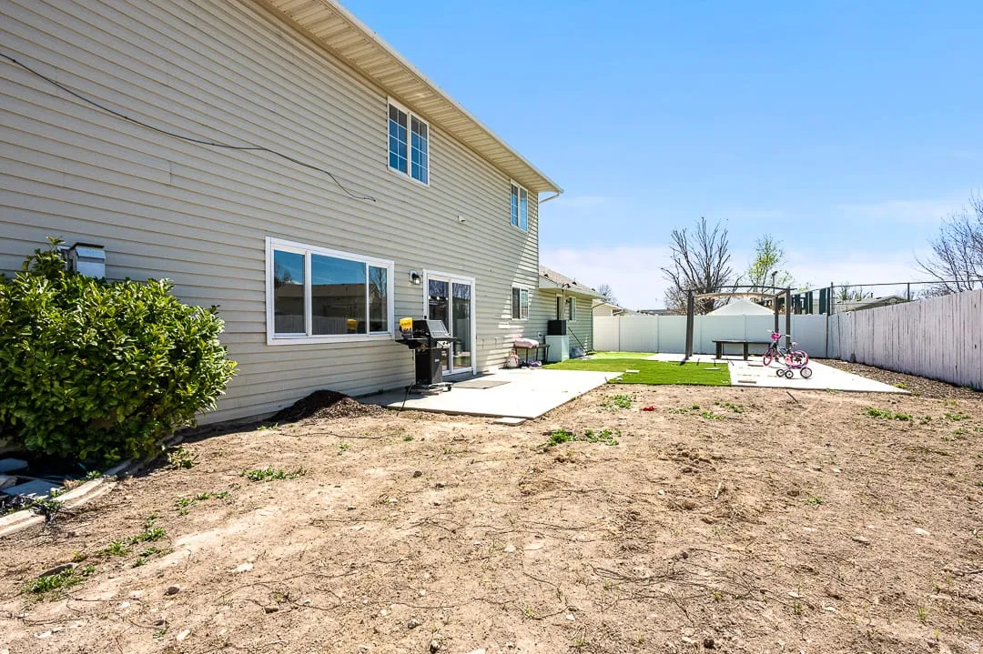 Expansive rear yard featuring a large concrete patio, artificial turf area, and perimeter fencing