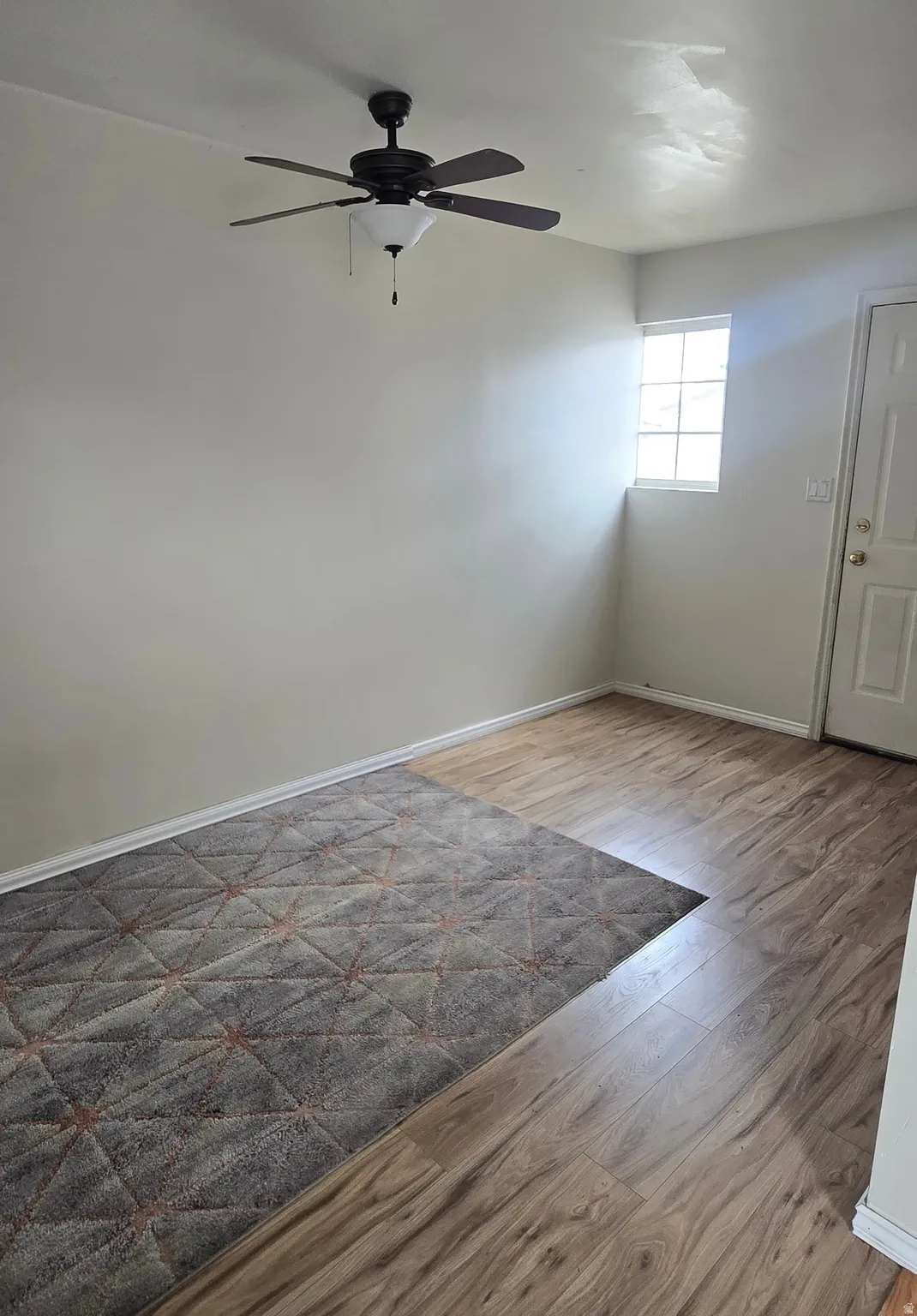 Room featuring wood-finish flooring, a ceiling fan with integrated lighting, and a single window with a grid pattern