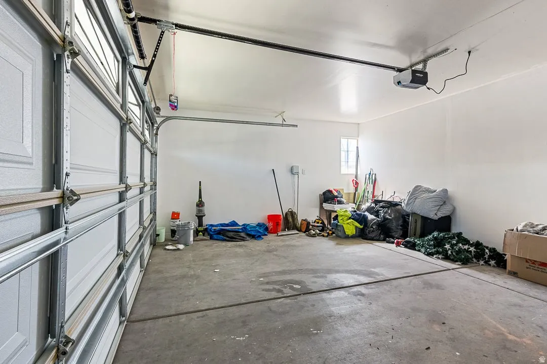 Interior garage space with a concrete floor, white painted walls, and an overhead garage door opener