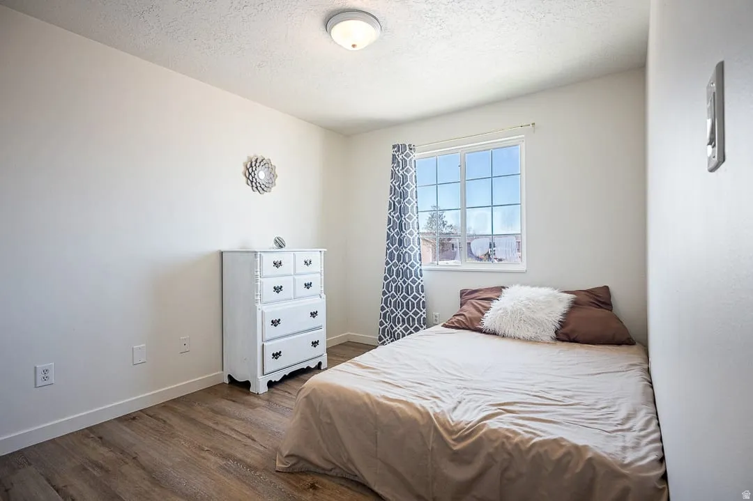 Bedroom featuring wood-finish flooring, white walls, a multi-pane window, and a flush-mount ceiling light fixture