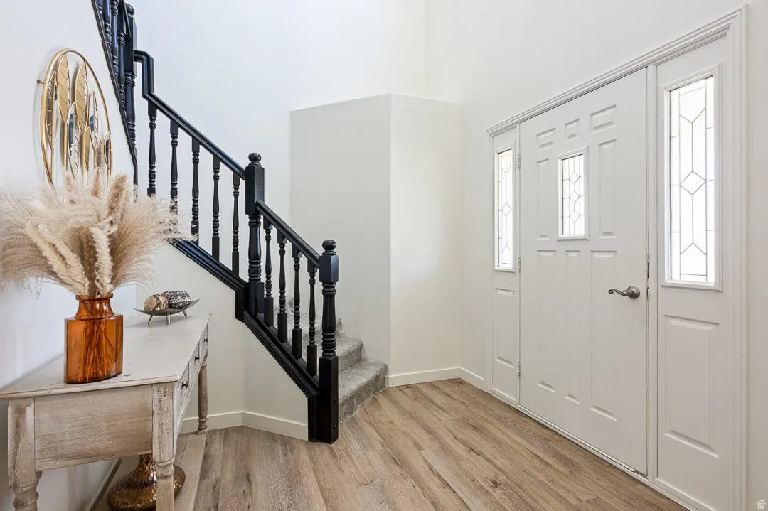 Foyer featuring wood-finish flooring, a white paneled entry door with decorative glass inserts, and a black painted staircase with carpeted treads