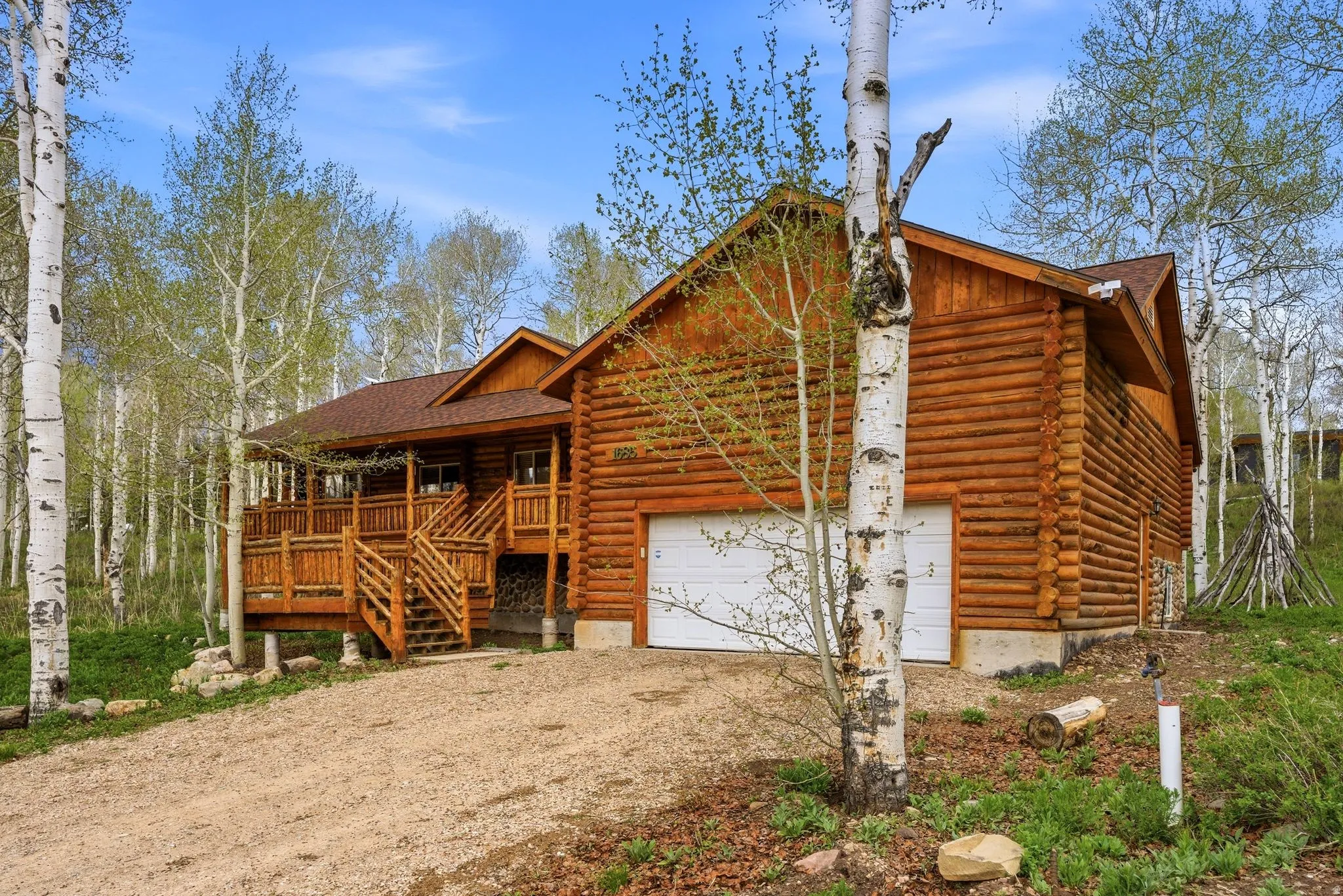 Log cabin exterior featuring a multi-level wooden deck, attached two-car garage, and surrounding mature trees