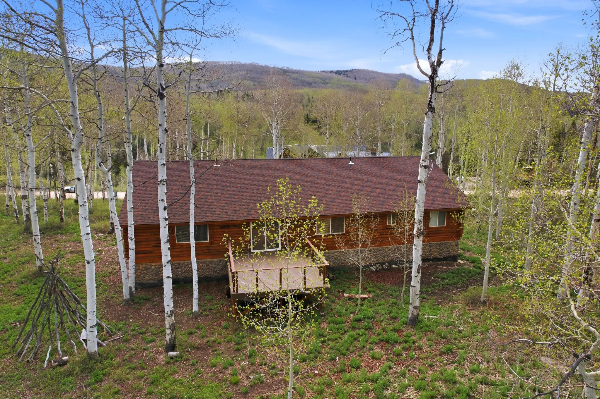 Wood-sided residence featuring a red shingle roof and a stone foundation