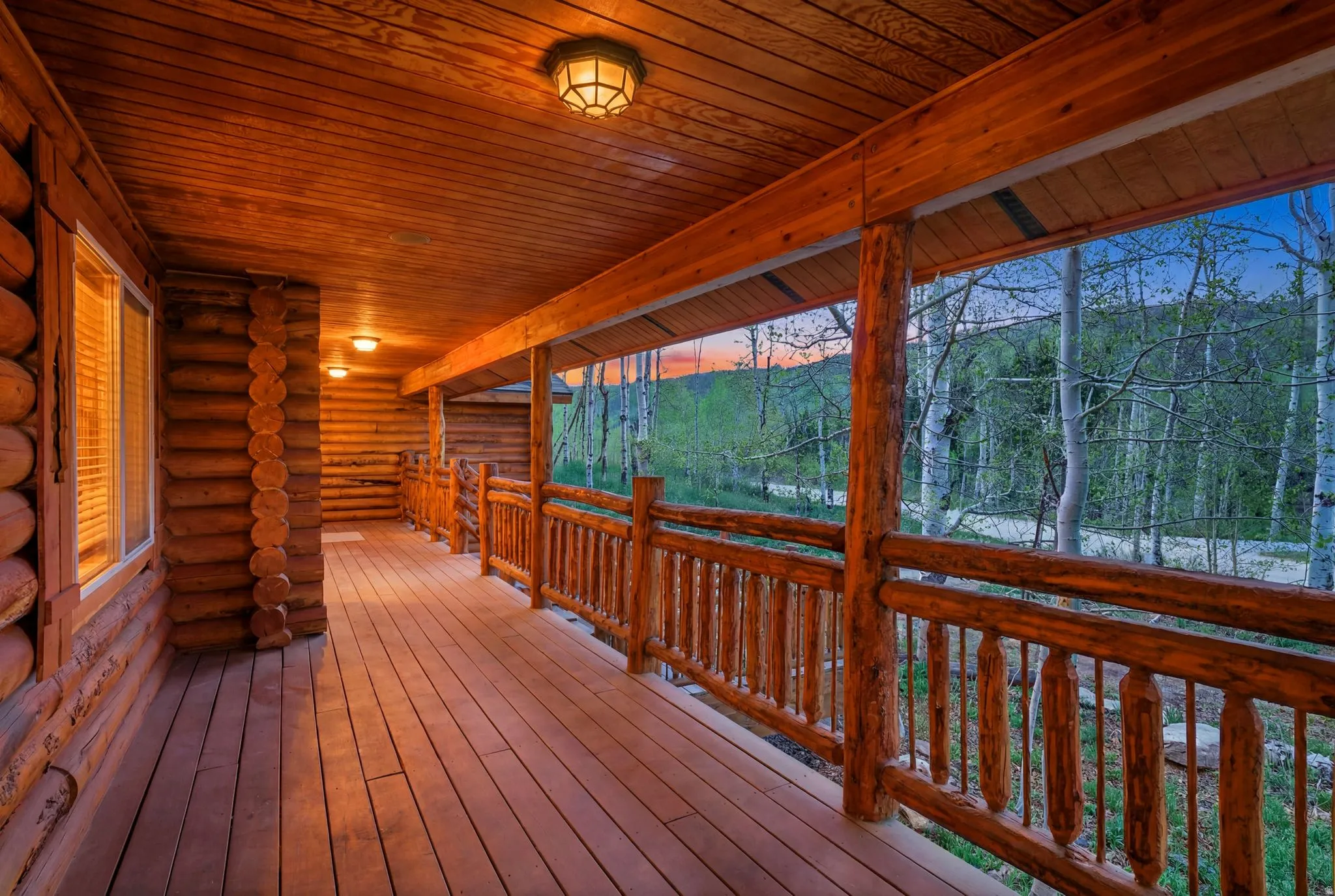 Expansive log cabin porch featuring natural wood flooring and railing, wood-paneled ceiling, integrated ceiling lighting, and a window with blinds