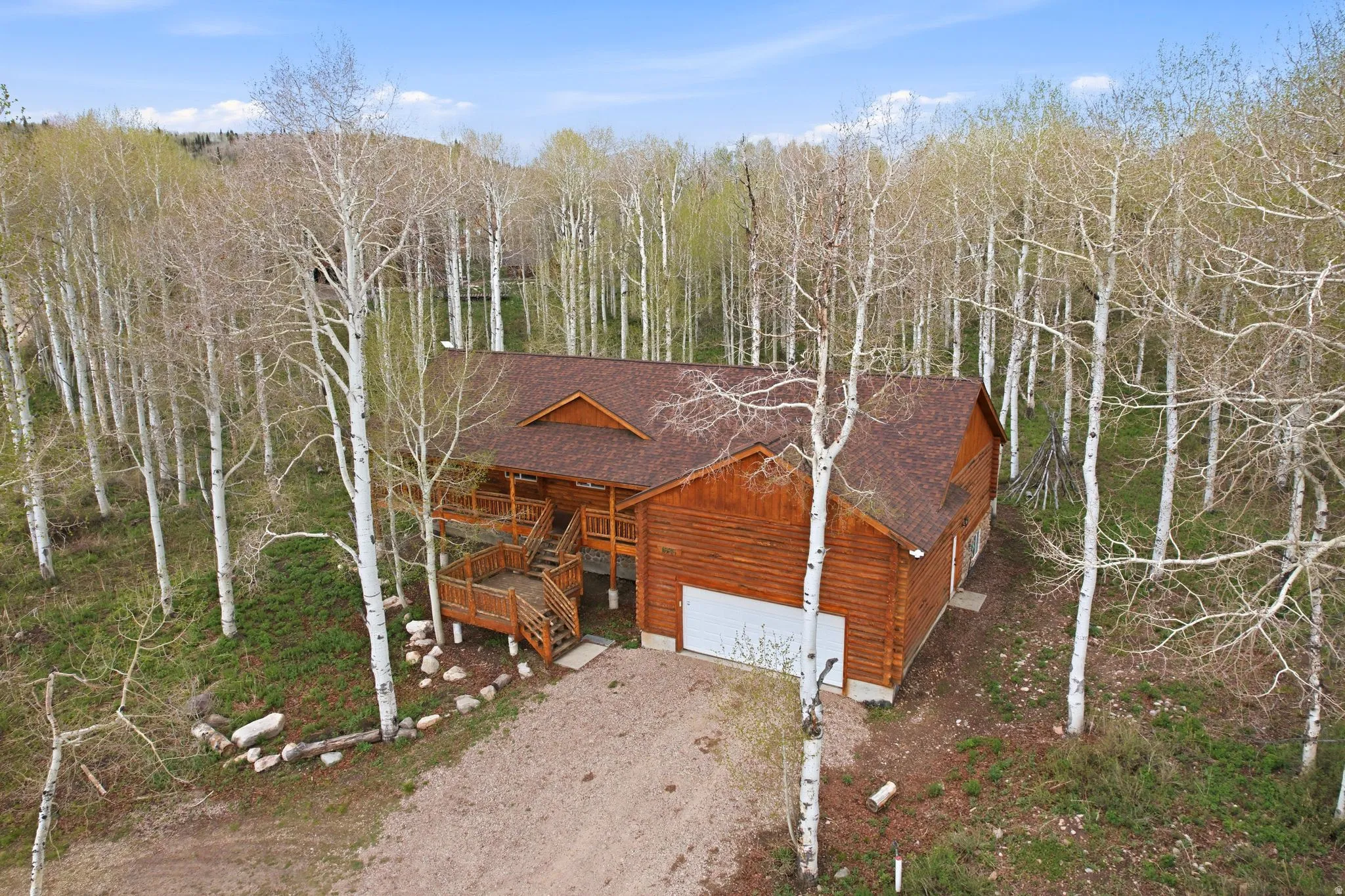 Log cabin architecture with multiple exterior decks, an integrated garage, and a brown shingle roof surrounded by aspen trees