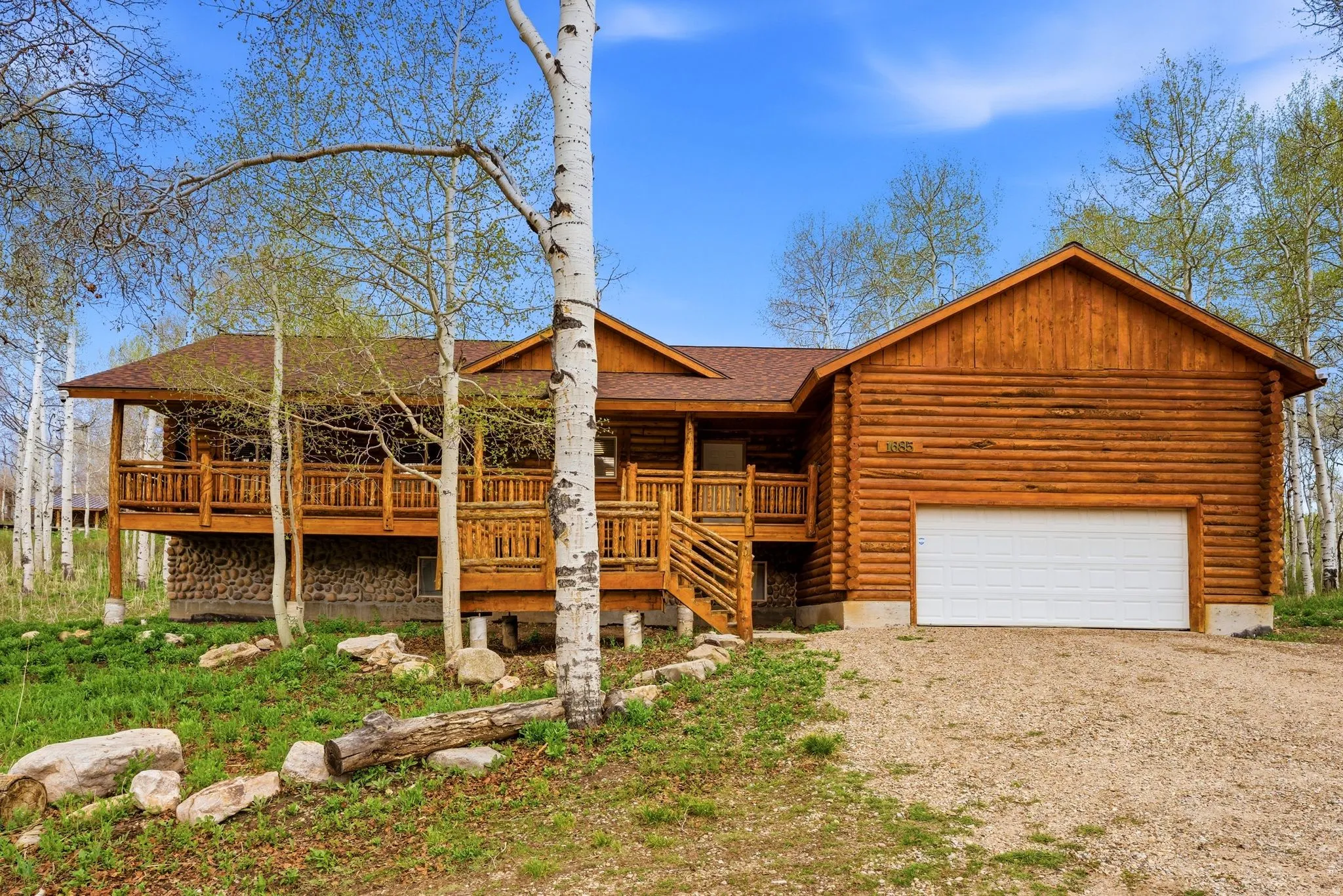 Rustic log cabin-style home featuring a full-width covered front porch with wood railings and steps