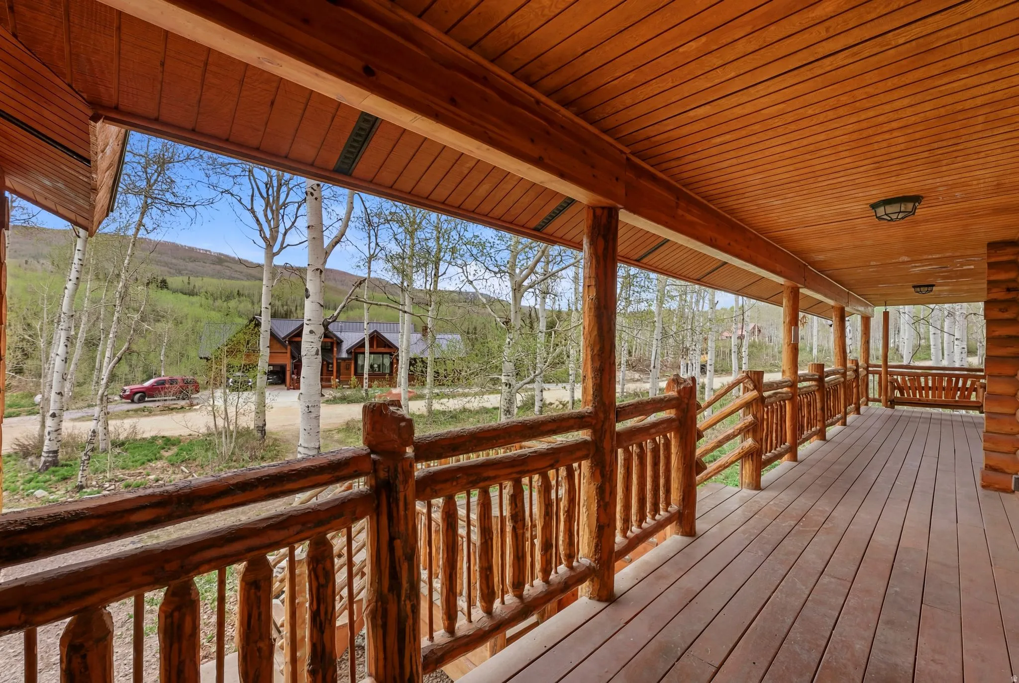 Expansive wood-plank porch with a log railing system and wood-paneled ceiling