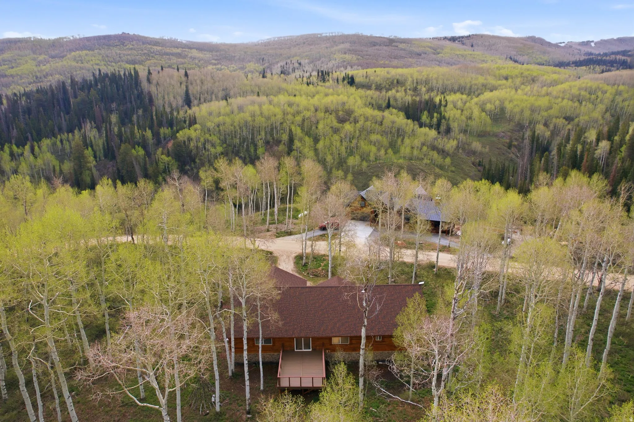 Expansive woodland property featuring a main residence with a large deck, surrounded by mature trees, and a separate structure with a dark roof