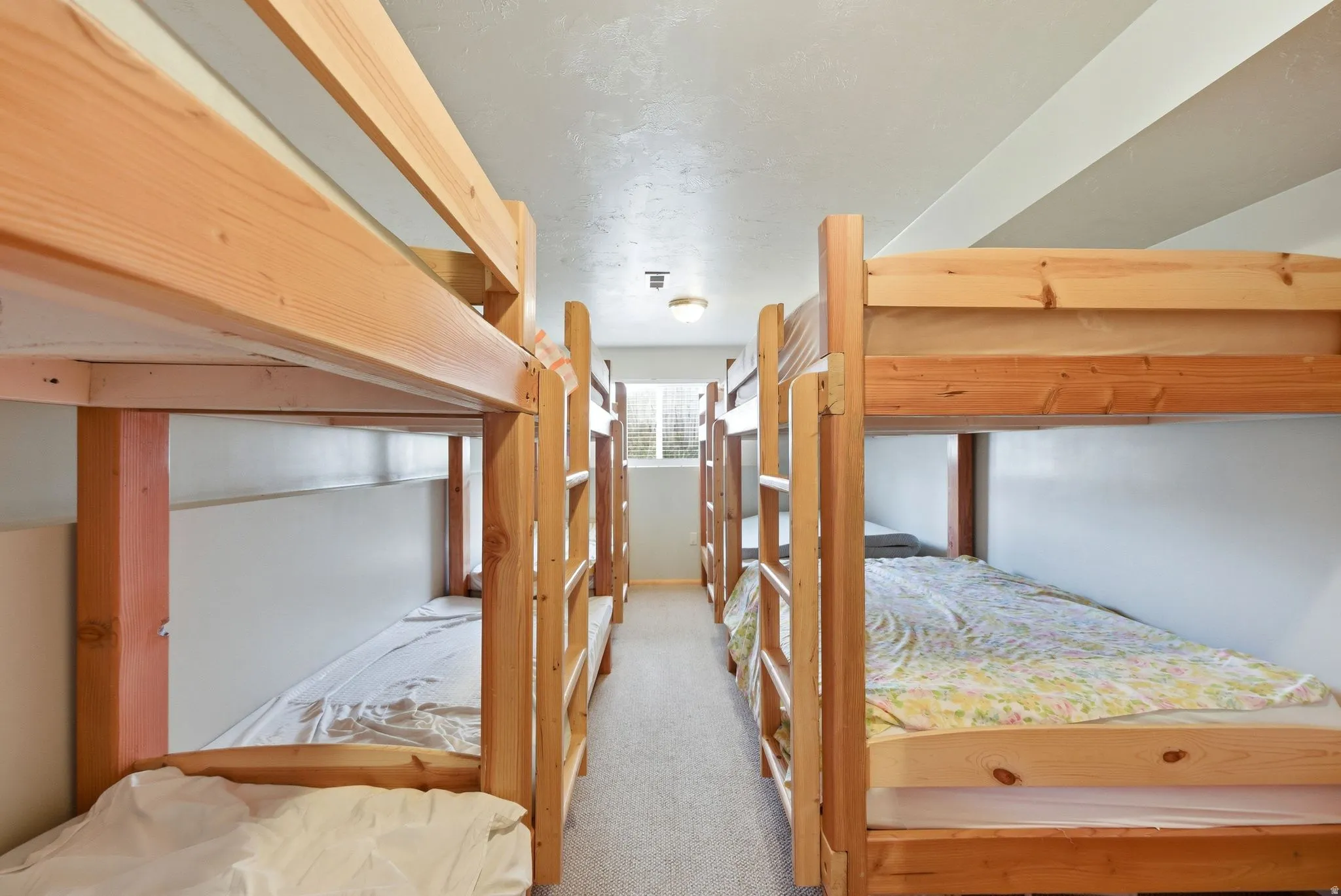 Room featuring multiple wooden bunk beds, neutral tone carpeting, and white walls