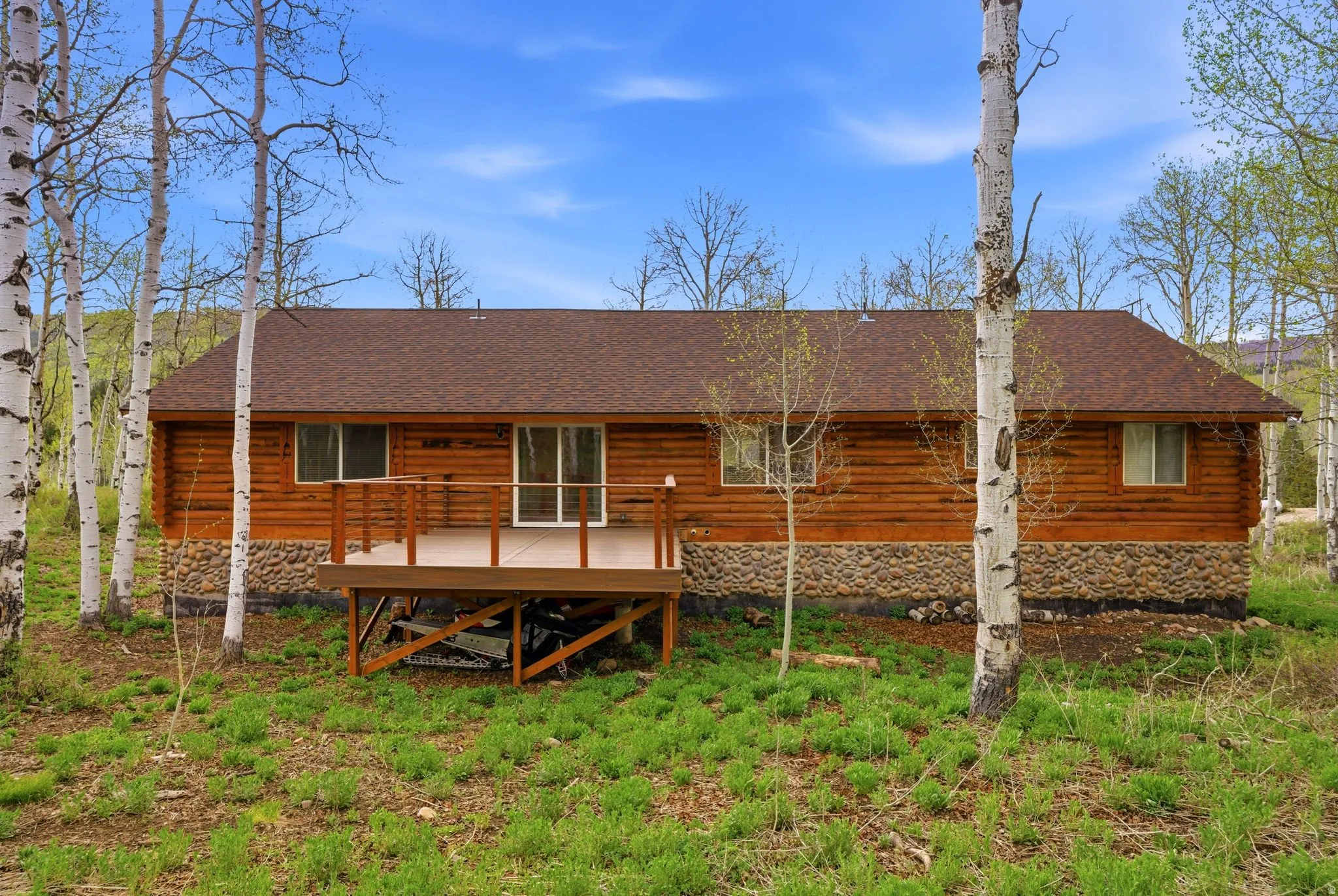 Log cabin exterior featuring a brown shingle roof, stone foundation, and wood siding